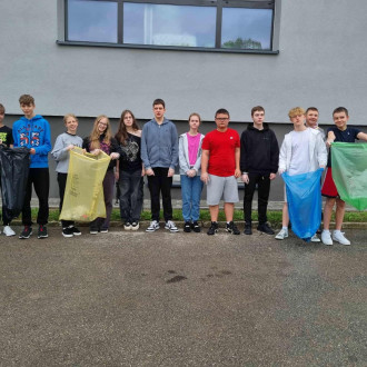 Uczniowie z klasy VIII stoją pod budynkiem szkoły i trzymają worki na śmieci. 