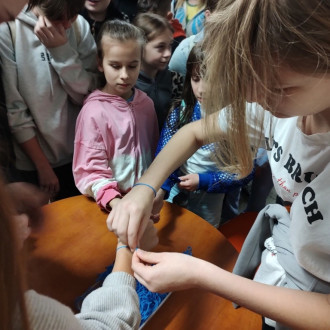 Uczniowie podczas wiązania niebieskiej nitki na nadgarstku