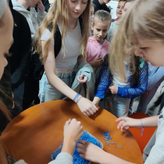 Uczniowie podczas wiązania niebieskiej włóczki